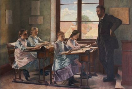 Ein Mann steht in einem Schulzimmer. Es sitzen vier Schülerinnen am Pult.