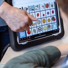 Hand zeigt auf Tablet mit Symbolen für Obst und Lebensmittel, Kind schaut darauf.