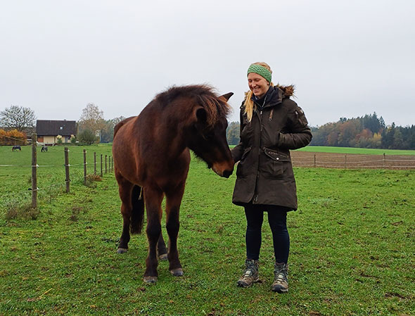 Lia Frankenbach hält ihre Hand an das Maul eines dunklen Pferdes.